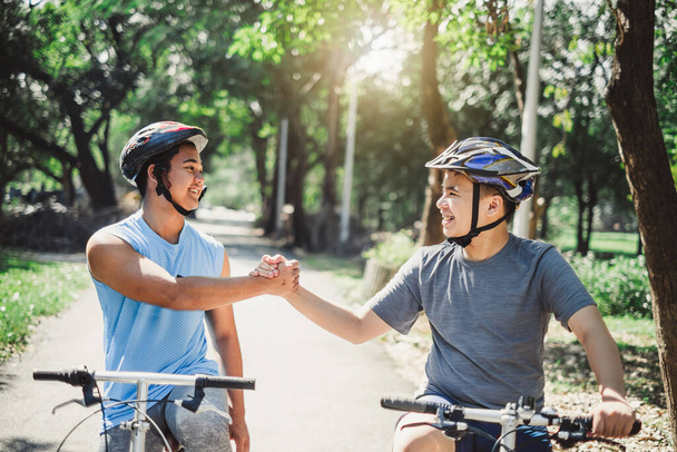 Asian boy with friend ride a bike/bicyle at outdoor green park in summer, teamwork concept - Photo, Image