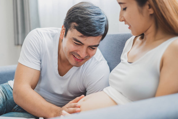 Νεαρός Ασιάτης σύζυγος αγγίζει / ακούει στην κοιλιά έγκυος γυναίκα με αγάπη και ευτυχισμένη - Φωτογραφία, εικόνα