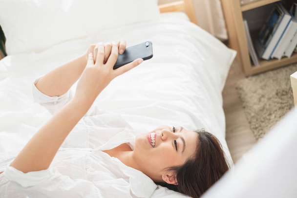 Schöne Asiatin mit Laptop und Smartphone im Schlafzimmer für Online-Shopping, asiatische Frau Lifestyle-Konzept - Foto, Bild