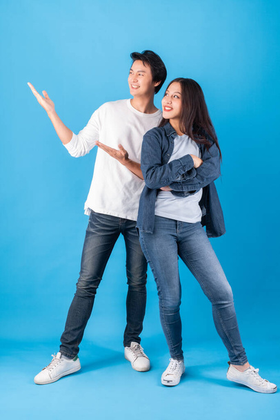 Junges asiatisches glückliches Paar, Mann und Frau, die mit offenen Händen Produkte auf blauem Hintergrund präsentieren, Studioaufnahme - Foto, Bild