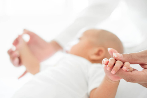 Genç Asyalı anne yeni doğmuş bebeğini beyaz yatakta sevgiyle tutuyor. Anneler günü konsepti. - Fotoğraf, Görsel