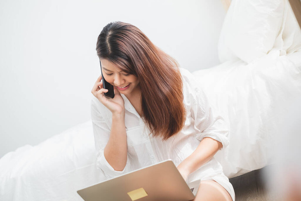 Belle femme asiatique utilisant ordinateur portable et téléphone intelligent dans la chambre à coucher pour les achats en ligne, concept de style de vie femme asiatique - Photo, image