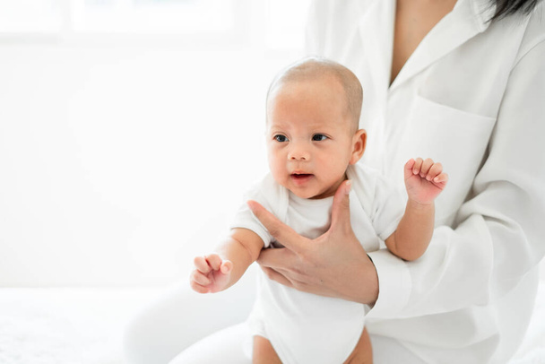 Fiatal ázsiai anya kezében újszülött baba szeretettel fehér ágyon, anyák napja koncepció - Fotó, kép