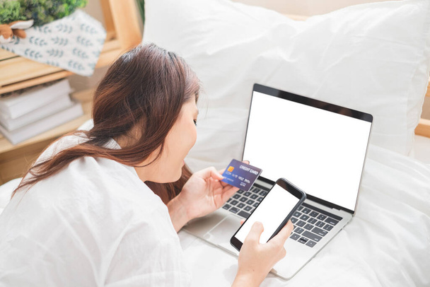 Hermosa mujer asiática que utiliza el ordenador portátil y el teléfono inteligente en la habitación de la cama para las compras en línea, concepto de estilo de vida mujer asiática - Foto, Imagen