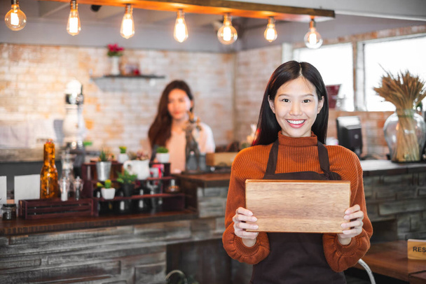 Joven mujer asiática propietaria de un negocio frente a una cafetería / bar / restaurante / cafetería y panadería - Foto, imagen