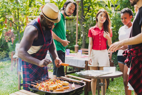 Група різноманітних людей, які влаштовують вечірку на барбекю/барбекю вдома, готують м'ясо/яловичину на обід, концепцію вечірки щасливих друзів
 - Фото, зображення