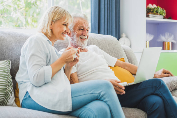 Пара пожилых людей с компьютером ноутбук на диване дома для онлайн-покупок, серфинг Интернет - Фото, изображение