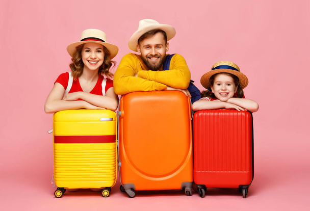 Optimistic parents and daughter leaning on luggage and smiling for camera during summer vacation against pink backdro - Photo, Image
