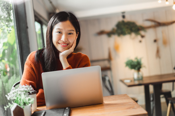 Kafede dizüstü bilgisayarda çalışan Asyalı genç iş kadını portresi. Gülümsüyor ve mutlu çalışıyor.. - Fotoğraf, Görsel