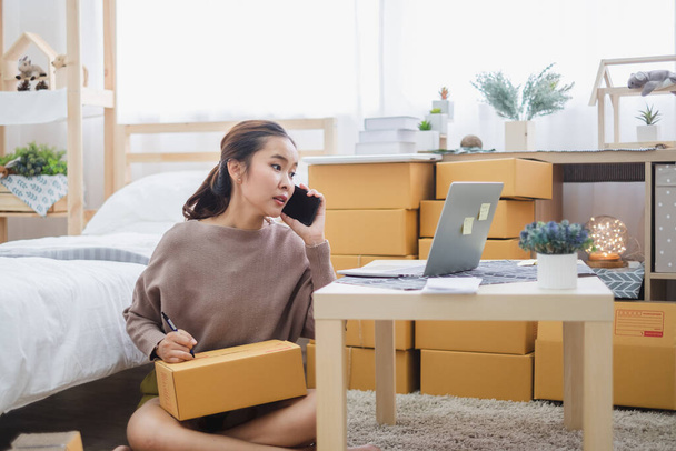 Młoda azjatycka kobieta sprzedawca rozmawiając telefon z klientem dla biznesu online, zakupy online, wysyłki, box i koncepcji pakietu. - Zdjęcie, obraz