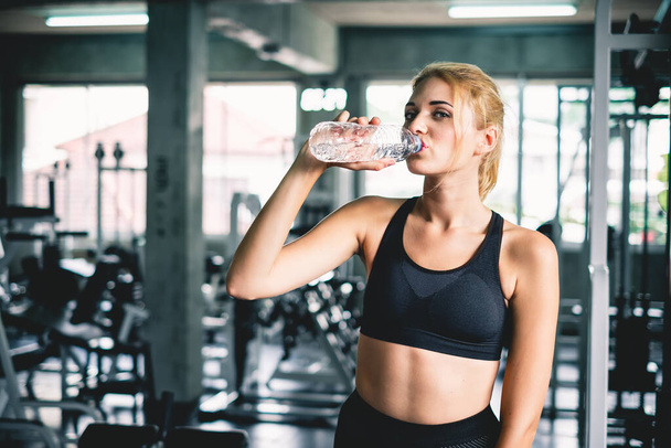 Mujer bebiendo agua después de terminar el entrenamiento en el gimnasio deportivo, con sonrisa feliz y relajarse - Foto, Imagen