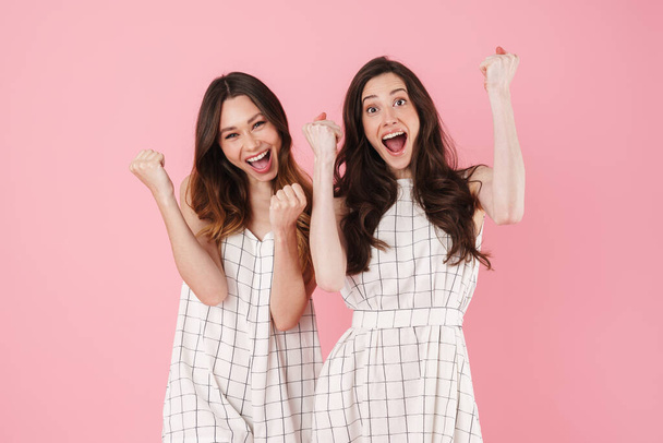 Image of excited caucasian women smiling and making winner gesture isolated over pink background - Foto, imagen