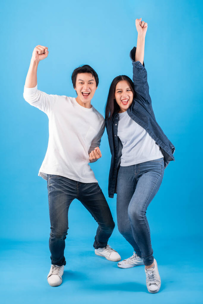 Excited young Asian couple man and woman happy celebrate success over blue background, winner concept - Фото, зображення