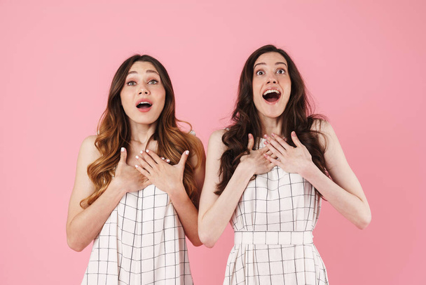 Image of astonished nice women expressing surprise with hands on their chests isolated over pink background - Фото, изображение