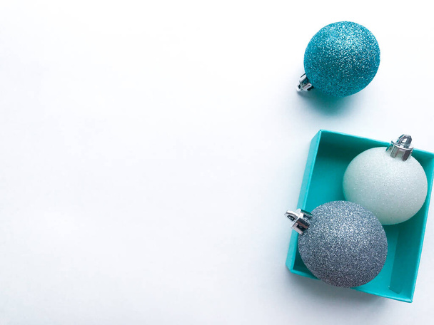 Close up of the turquoise (blue) gift box with shiny Christmas ball of silver. Blue and white lie near. White background. The spirit of the coming Christmas and new year - Photo, Image