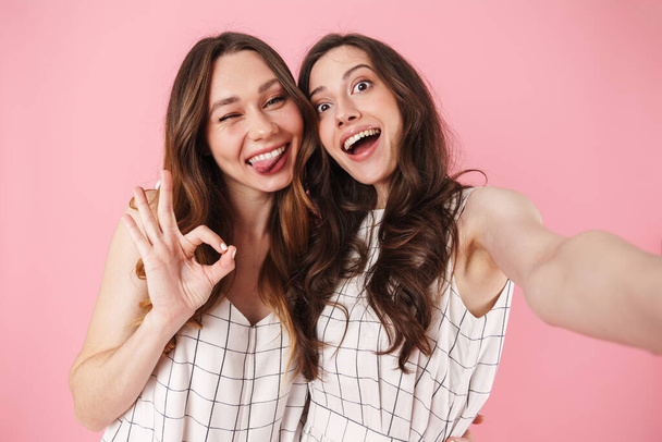 Image of funny women waving gesturing ok sign while taking selfie photo isolated over pink background - Fotoğraf, Görsel
