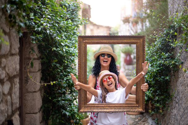 A Mother and her daughter in the antique frame at the streets of Eze, France , travel concept with frame - Photo, Image