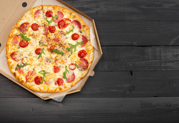 top view of pizza with tomatoes, salami and cheese in box on wooden table - Foto, Imagem