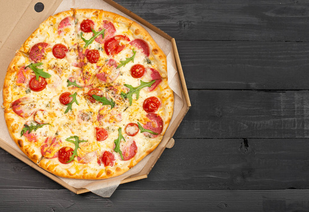 top view of pizza with tomatoes, salami and cheese in box on wooden table - Valokuva, kuva