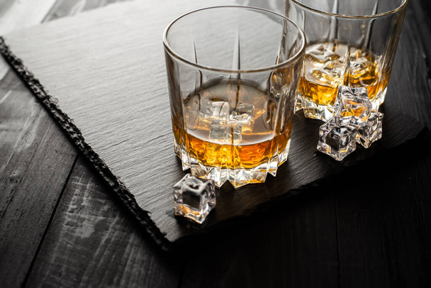 close-up view of glasses of whisky and ice cubes on wooden table - Foto, imagen