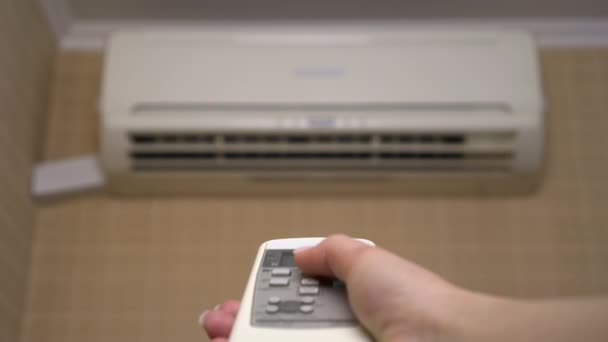 Ilmastointi talossa säätää huoneenlämpötilaa. Nainen sammuttaa ilmastoinnin kaukosäätimellä. Lähemmäs. Ilmastointilaite epäselvä - Materiaali, video