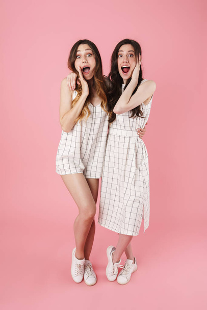 Image of delighted attractive women expressing surprise while hugging isolated over pink background - Foto, afbeelding