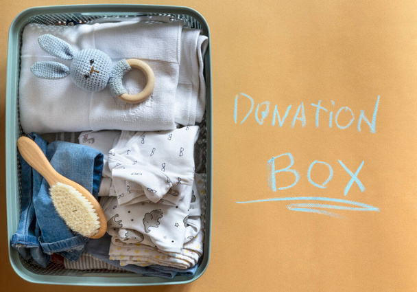 Karamel arka planında çocuk oyuncakları ve kumaş olan plastik bağış kutusu. Üst manzara, düz uzanma - Fotoğraf, Görsel