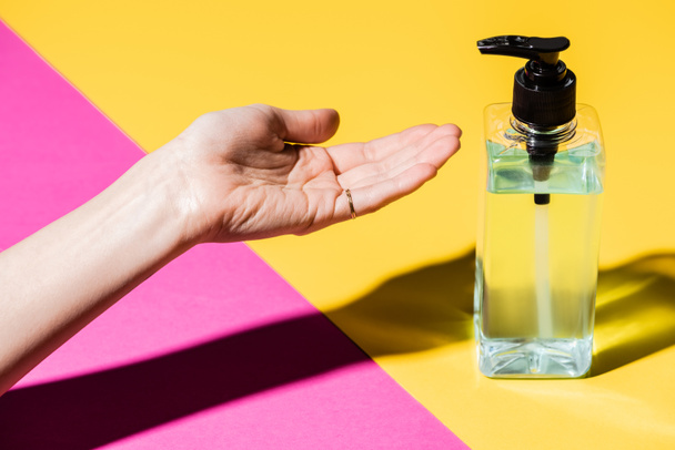 cropped view of female hand near bottle with liquid antiseptic on pink and yellow - 写真・画像