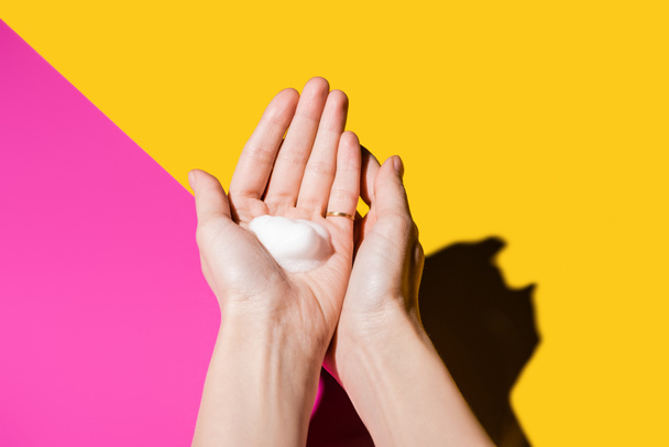 częściowy widok żeńskich rąk z pianką mydlaną na różowo-żółtym - Zdjęcie, obraz