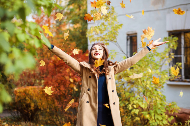 Stylish woman is throwing up autumn leaves, having fun outdoors in fall season.  - Фото, изображение