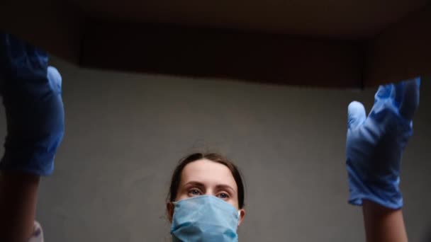 Shot from below of brunette woman in medical face mask and latex gloves carefully opened box delivery from online store. Concept coronavirus pandemic quarantine, home isolation self, social distance - Filmati, video