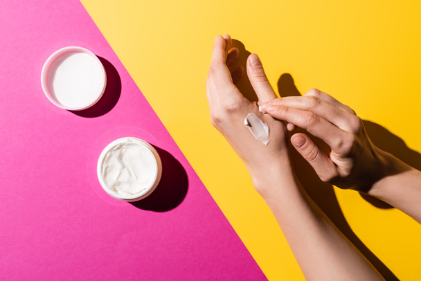 cropped view of woman applying hand cream on pink and yellow - Foto, afbeelding