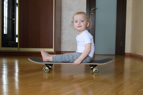 child rides a frame on a skateboard. Little girl on a board rolls around the house - Фото, зображення