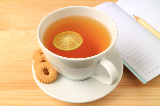 Xícara de chá de limão quente com biscoitos e papéis de nota alinhados na mesa de madeira
 - Foto, Imagem