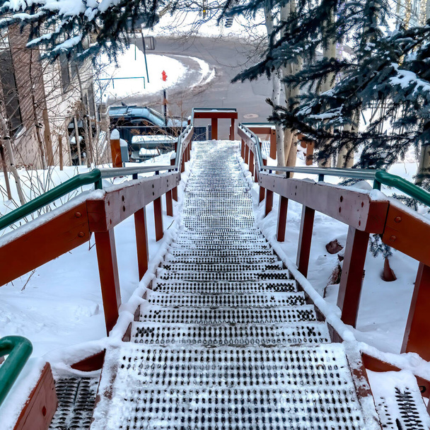 Quadratischer Rahmen Treppe und Straße auf schneebedecktem Hügel inmitten von Häusern und Nadelbäumen - Foto, Bild