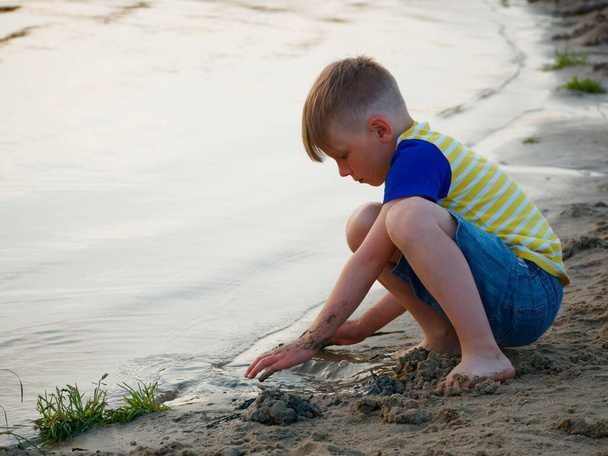 boy plays with sand on the beach near the water 2020 - Photo, image