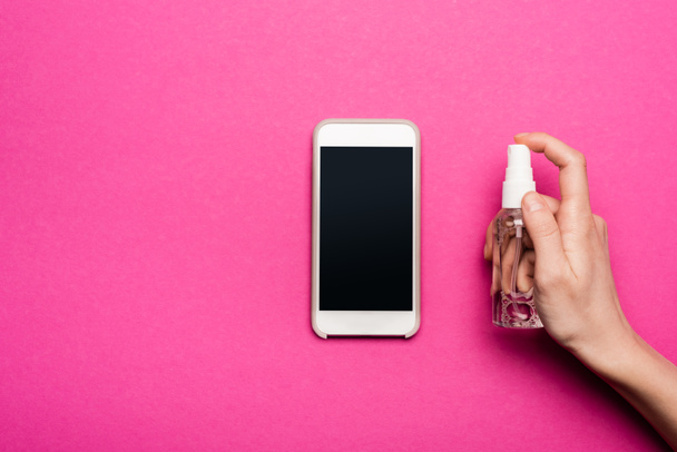 partial view of woman spraying antiseptic on smartphone with blank screen on pink - Foto, imagen