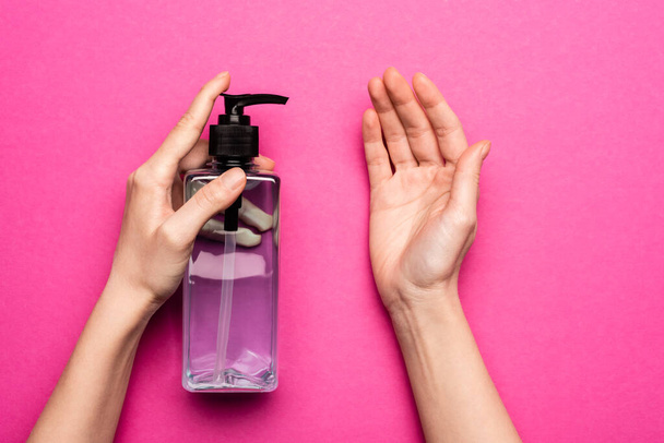 przycięty widok kobiety stosującej środek dezynfekujący na ręce na różowo - Zdjęcie, obraz