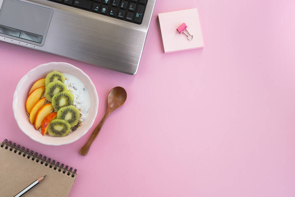 Healthy food on working table. Muesli with natural yogurt, peach and kiwi on light pink background. Snack at workplace, food in the office. Top view, flat lay, copy space - Foto, Bild