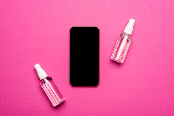 widok z góry butelki z płynem antyseptycznym w pobliżu smartfona z pustym ekranem na różowym - Zdjęcie, obraz