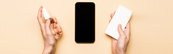 horizontales Bild weiblicher Hände mit Desinfektionsmittel und Papierservietten in der Nähe von Smartphones mit leerem Bildschirm auf beige - Foto, Bild