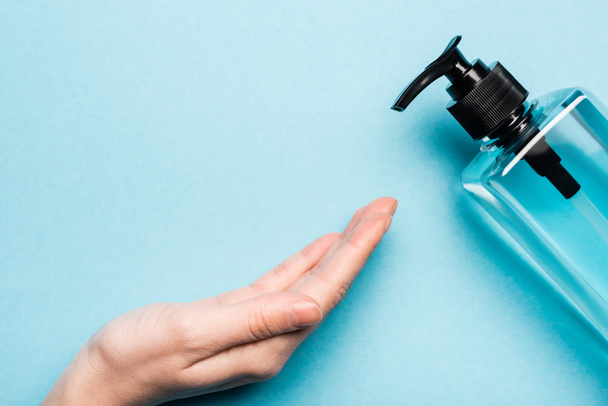 partial view of female hand near bottle with sanitizer on blue - Photo, Image