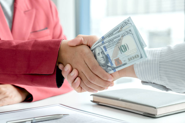 photo of Businessmen shake hands and dollar note, sign a contract to bribe corruption in the company. The concept of bribery and corruption. - Photo, Image