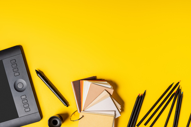 top view of drawing tablet, colorful palette and pencils near stylus on yellow - Foto, afbeelding