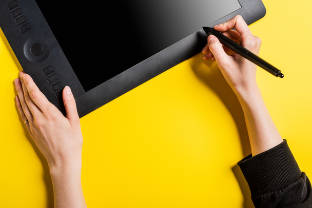 przycięty widok projektanta trzymającego czarny rysik w pobliżu tabletu rysunkowego z białym ekranem na żółtym  - Zdjęcie, obraz