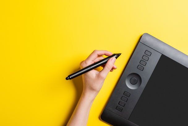 cropped view of designer holding stylus near drawing tablet with blank screen on yellow  - Fotoğraf, Görsel