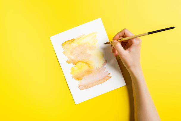 vista ritagliata di artista che tiene pennello vicino alla pittura su giallo
  - Foto, immagini