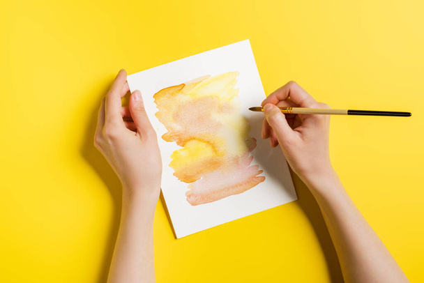 cropped view of woman holding paintbrush near painting on yellow  - Zdjęcie, obraz