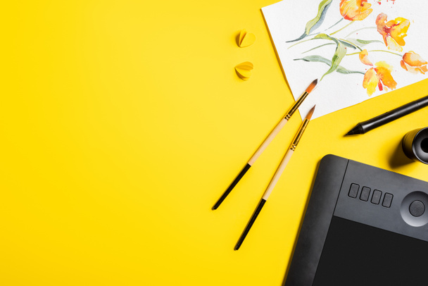 vista superior de pincéis perto da pintura, elementos de corte de papel, tablet de desenho e estilete em amarelo
  - Foto, Imagem
