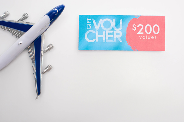 Top view of toy plane near gift voucher with 200 values sign on white background - Foto, afbeelding